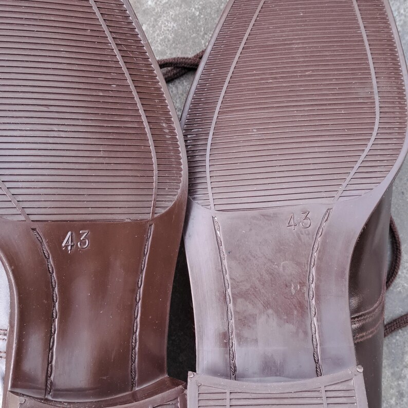 May include: Close-up of the soles of two brown leather shoes. The soles have a textured pattern and the number "43" is visible on each sole. The shoes appear to be new.