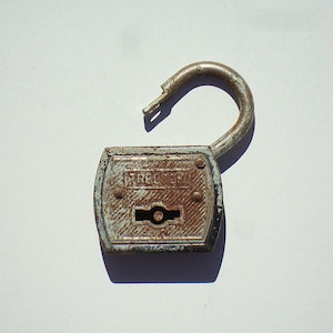 May include: An open, vintage padlock with a rusty, distressed appearance. The metal lock has a light blue and brown color scheme, with the word "TRECOCK" visible on the front. The lock's shackle is open, suggesting it is unlocked.