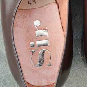 May include: Close-up of a brown leather shoe interior. The insole is a light brown color with a silver logo that reads "Sir". The number "43" is visible near the top of the shoe.
