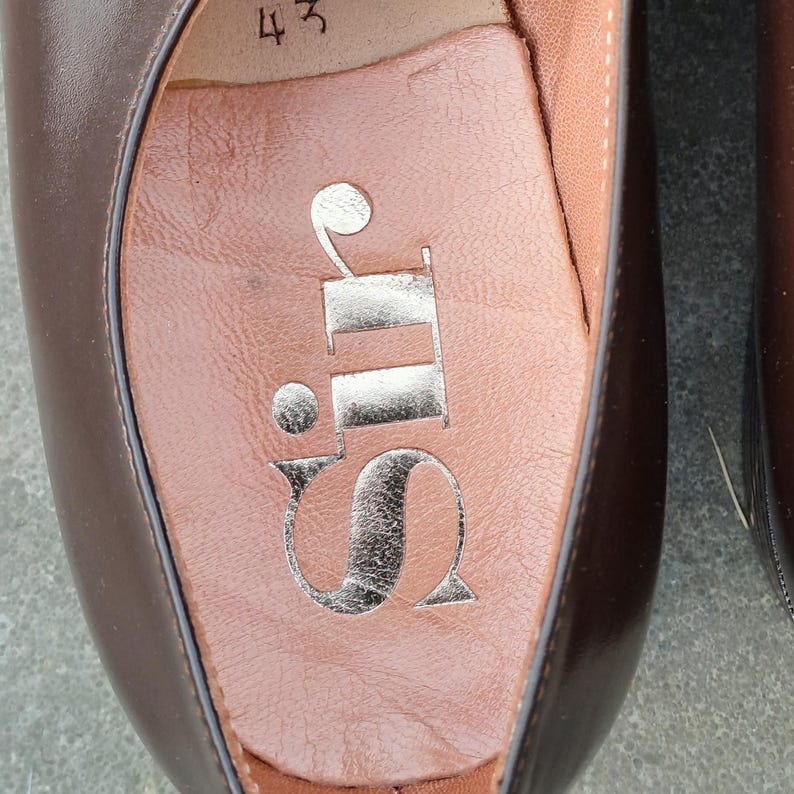 May include: Close-up of a brown leather shoe interior. The insole is a light brown color with a silver logo that reads "Sir". The number "43" is visible near the top of the shoe.