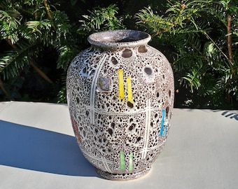 May include: A decorative ceramic vase with a speckled brown and white pattern. The vase features a grid design with colorful accents, including yellow, blue, and green vertical lines. The vase has a wide body and a narrow neck.