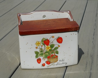 May include: A ceramic wall-mounted spice rack with a wooden lid. The rack is decorated with a "Wild Strawberry" design featuring red strawberries, yellow flowers, and a wicker basket. The rack is beige with brown speckles.
