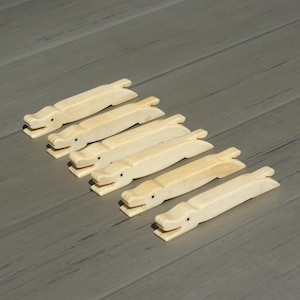 May include: Six cream-colored, carved alligator-shaped objects with small black eyes are arranged diagonally on a gray wooden surface. The alligator figures have open mouths and detailed features.