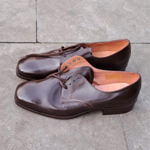 May include: A pair of brown leather dress shoes with a rounded toe and lace-up closure. The shoes have a polished finish and a light brown interior. The shoes are displayed on a gray surface.