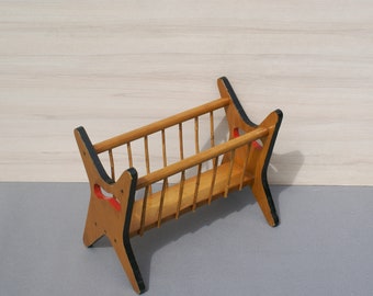 May include: A vintage wooden magazine rack with a light brown finish. The rack features a slatted design with vertical supports and curved side panels with black trim and red accents. The rack is designed to hold magazines or newspapers.
