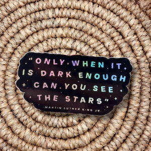May include: A black sticker with the quote "ONLY WHEN IT IS DARK ENOUGH CAN YOU SEE THE STARS" by Martin Luther King Jr. The text is in a colorful, iridescent font with a starry design.