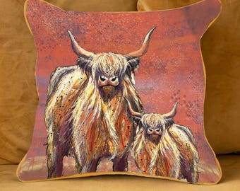 May include: Square decorative pillow featuring a watercolor painting of two Highland cows. The pillow has a rust-colored background with a gold trim. The cows have long, shaggy fur in shades of brown, tan, and white.