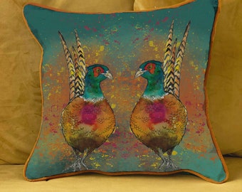 May include: A teal blue throw pillow with a brown border features a watercolor illustration of two colorful pheasants facing each other on a background of orange, yellow, and pink splatters.