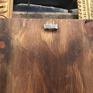 May include: A close-up of a brown wooden board with a silver metal hanging hook attached to the back.