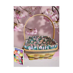 May include: A woven wooden basket with a single arched handle and a fabric liner featuring a colorful pattern of Easter eggs. Beside the basket stands a small rectangular product card with the text 1988 Easter Basket printed on the front cover.