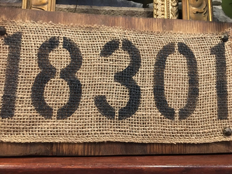 May include: A rustic wooden sign with the number 18301 printed on a hessian background. The sign is secured with metal tacks.
