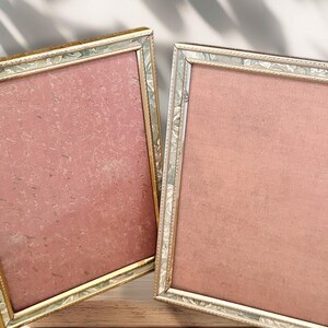 以下が含まれることがあります： ピンクがかった赤色の背景を持つ2つの長方形のフォトフレーム。フレームは、装飾的な花のパターンを持つ金と銀色のトリムが付いています。フレームは空で、写真やアートワークの準備ができています。