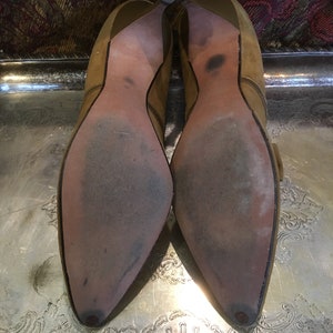 May include: A pair of brown suede heeled shoes with pointed toes. The shoes have a buckle detail on the side and are worn.