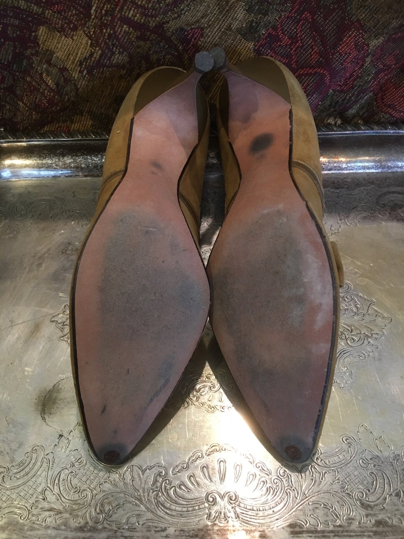 May include: A pair of brown suede heeled shoes with pointed toes. The shoes have a buckle detail on the side and are worn.