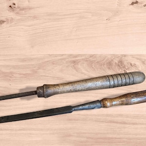 May include: Two antique woodworking tools with wooden handles. One is a long, slender awl with a cylindrical handle. The other is a chisel with a flat, rectangular blade and a shorter, rounded handle. Both tools show signs of wear.