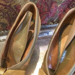 May include: A pair of brown suede shoes with a bow on the front. The shoes have a leather lining and a leather sole.