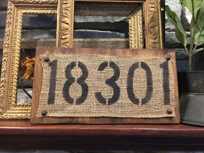 May include: A rustic wooden sign with a burlap background and black stenciled numbers reading "18301".
