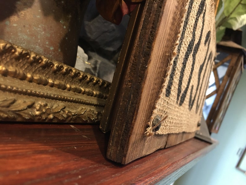 May include: A rustic wooden sign with the word "Welcome" printed on burlap fabric. The sign is attached to a wooden frame and has a distressed look.