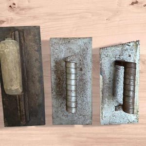Puede incluir: Tres llana de acabado de hormigón vintage con mangos de madera y metal. Las llanas son rectangulares con un aspecto desgastado y envejecido, mostrando signos de uso. Los mangos son cilíndricos.