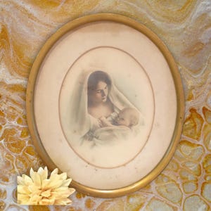 May include: A framed vintage print of a mother and child. The mother is wearing a white robe and holding a baby in her arms. The print is in a gold oval frame.