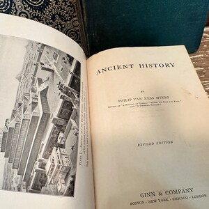 Puede incluir: Un libro abierto titulado "Ancient History" de Philip Van Ness Myers. El libro es una edici&oacute;n revisada y publicado por Ginn & Company. El libro est&aacute; abierto en una p&aacute;gina con una ilustraci&oacute;n en blanco y negro de un edificio.