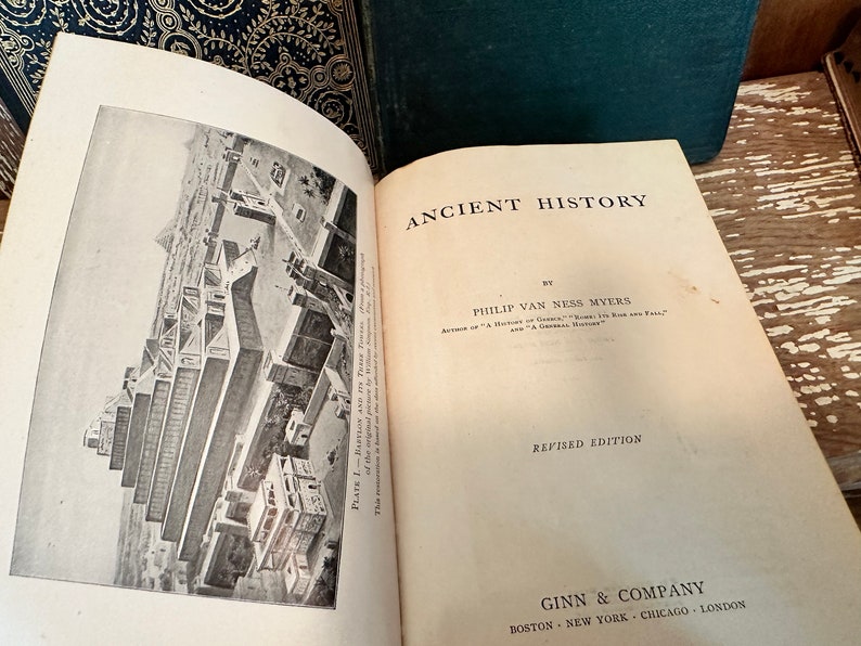 Puede incluir: Un libro abierto titulado "Ancient History" de Philip Van Ness Myers. El libro es una edici&oacute;n revisada y publicado por Ginn & Company. El libro est&aacute; abierto en una p&aacute;gina con una ilustraci&oacute;n en blanco y negro de un edificio.