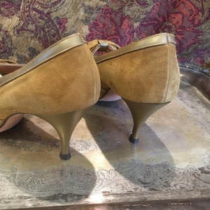 May include: A pair of brown suede heeled shoes with gold trim. The shoes have a peep toe and a bow detail on the front.
