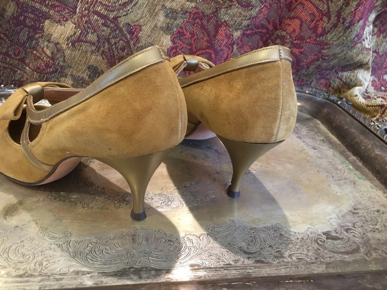May include: A pair of brown suede heeled shoes with gold trim. The shoes have a peep toe and a bow detail on the front.