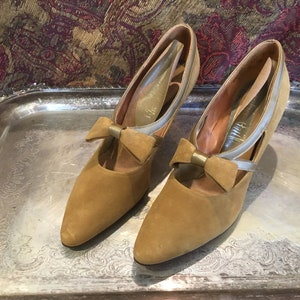 May include: A pair of brown suede heeled shoes with a gold bow accent and a silver strap detail.