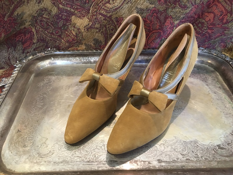 May include: A pair of brown suede heeled shoes with a gold bow accent and a silver strap detail.