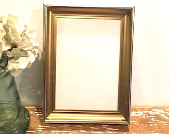 Op de afbeelding: Een gouden fotolijst met een witte passe-partout en een witte achtergrond. De lijst staat op een houten oppervlak.