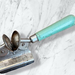 Peut inclure: Une cuillère à crème glacée vintage avec une cuillère en métal et une poignée en bois bleu clair. La cuillère a une base rectangulaire avec le texte "BURLINGTON, IA. SURE-SHARP No."