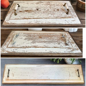 Op de afbeelding: Een rechthoekig houten dienblad met een witte verflaag en zichtbare houtnerf. Het dienblad heeft een bruine rand en decoratieve handgrepen. De afgesleten verf geeft het een rustieke, vintage uitstraling.