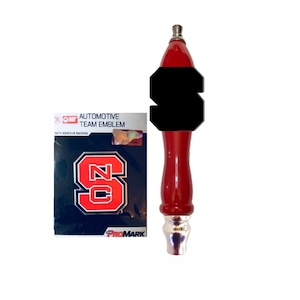 May include: A red and black tap handle with a silver base and a black emblem. Beside it is a navy blue automotive team emblem with a red and white "S" logo.