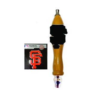 May include: A wooden beer tap handle with a chrome base and a black and orange San Francisco Giants logo sticker. The sticker says "Team Emblem Aluminum Color".