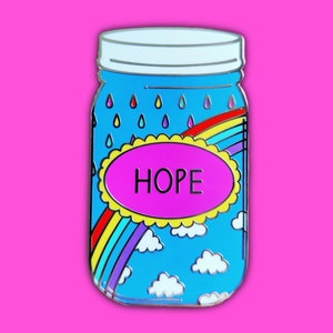 May include: A blue glass jar with a silver lid, featuring a rainbow, clouds, and raindrops. The jar has a yellow oval with the word "HOPE" in pink letters.