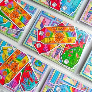 May include: A collection of colorful stickers featuring juice box designs with rainbow and fruit illustrations. The stickers have text like "Crushing It! Juice" and "Creative Juice". The stickers are packaged in clear plastic.