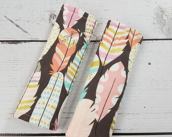 May include: Two fabric covered handles with a feather and dot pattern in pink, teal, and gold on a brown background.