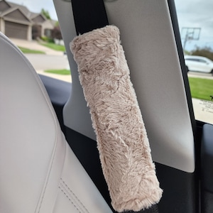 Puede incluir: Una funda para cintur&oacute;n de seguridad de coche de piel sint&eacute;tica beige. La funda est&aacute; unida a un cintur&oacute;n de seguridad negro.