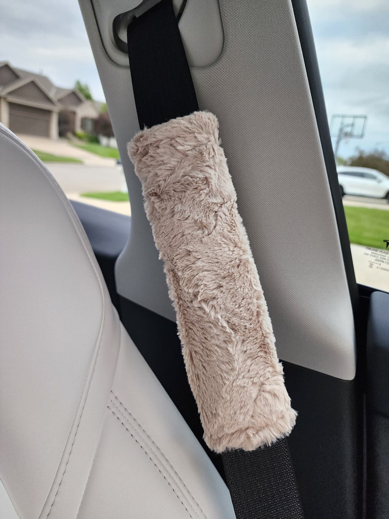 Puede incluir: Una funda para cintur&oacute;n de seguridad de coche de piel sint&eacute;tica beige. La funda est&aacute; unida a un cintur&oacute;n de seguridad negro.