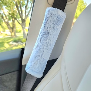 Puede incluir: Una funda para cintur&oacute;n de seguridad de coche de color azul claro y peluda. La funda est&aacute; hecha de un tejido suave y afelpado y est&aacute; dise&ntilde;ada para proteger el cintur&oacute;n de seguridad del desgaste.