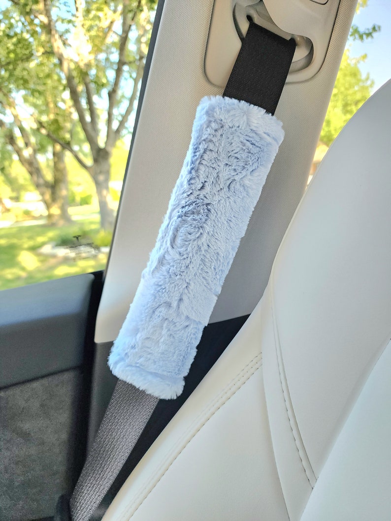 Puede incluir: Una funda para cintur&oacute;n de seguridad de coche de color azul claro y peluda. La funda est&aacute; hecha de un tejido suave y afelpado y est&aacute; dise&ntilde;ada para proteger el cintur&oacute;n de seguridad del desgaste.