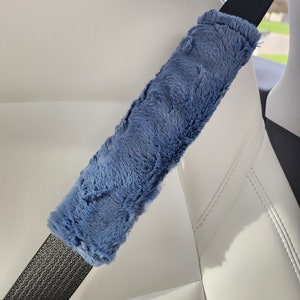 Puede incluir: Un coj&iacute;n de hombro para cintur&oacute;n de seguridad de felpa azul. El coj&iacute;n est&aacute; hecho de un material suave y peludo y est&aacute; dise&ntilde;ado para brindar comodidad y apoyo mientras se conduce.