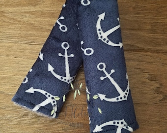 May include: A pair of navy blue fabric car seat belt covers with a white anchor pattern.