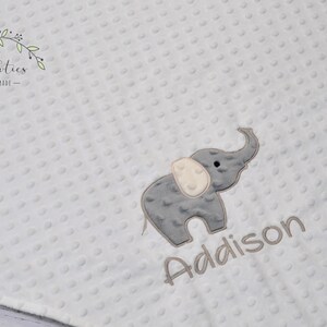 Puede incluir: Una manta de beb&eacute; blanca con un elefante bordado en gris y el nombre "Addison" en bordado gris.