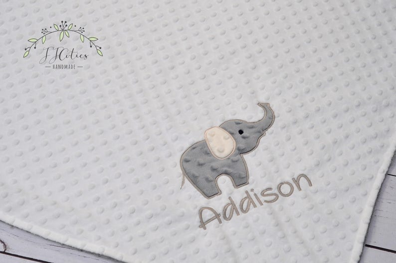 Puede incluir: Una manta de beb&eacute; blanca con un elefante bordado en gris y el nombre "Addison" en bordado gris.