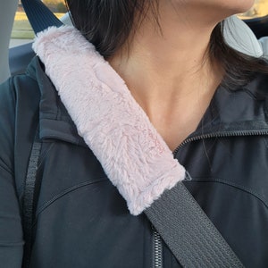 Puede incluir: Una funda para cintur&oacute;n de seguridad de coche de piel sint&eacute;tica rosa. La funda est&aacute; unida a un cintur&oacute;n de seguridad negro.