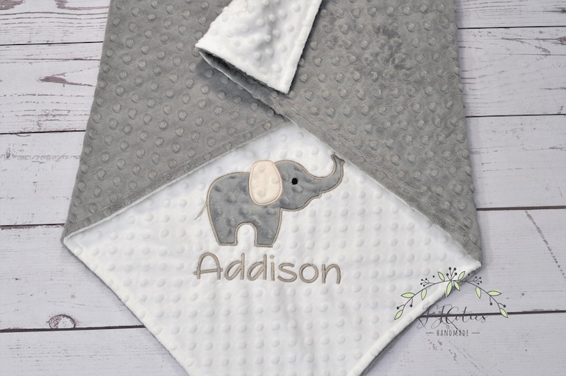 Puede incluir: Una manta de beb&eacute; gris y blanca con un elefante gris y el nombre Addison bordado en ella.