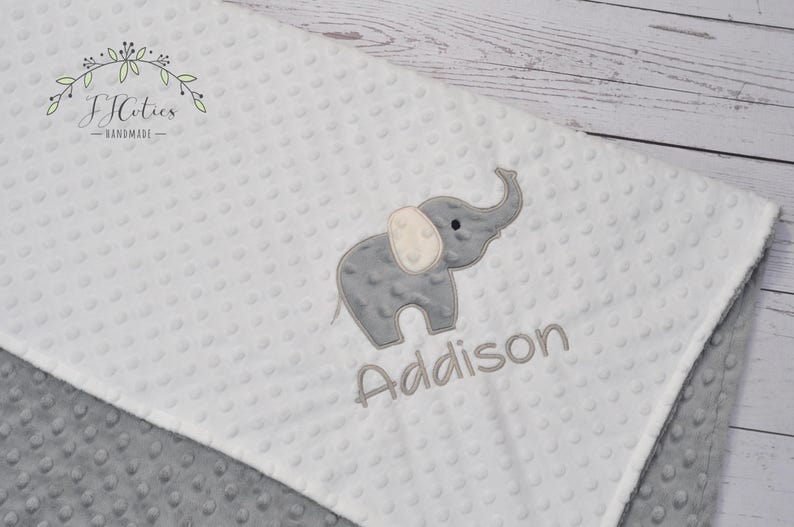 Puede incluir: Una manta de beb&eacute; blanca y gris con un elefante bordado gris y el nombre Addison.