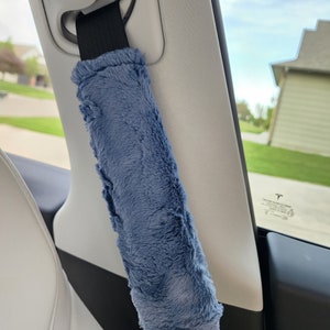 Puede incluir: Una funda de cintur&oacute;n de seguridad de coche de felpa azul. La funda est&aacute; unida a un cintur&oacute;n de seguridad negro y est&aacute; en un coche.